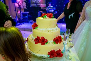 Elegant wedding cake with red rose decorations under dramatic purple and blue lighting.