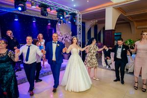 Panoramic view of wedding guests dancing in formal attire under blue and purple stage lighting.