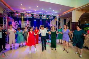 Group of dancers performing a line dance in a colorfully lit ballroom with overhead lighting and stage equipment.