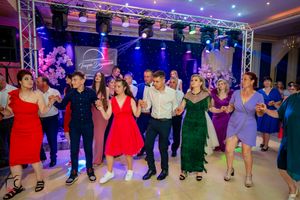 Group dance performance in a ballroom with professional lighting and staging equipment overhead.