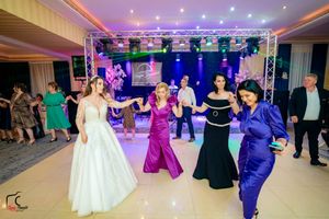 Guests line up for a group dance under purple and blue lighting at an elegant indoor venue.