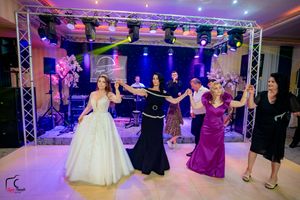 Wedding party performs choreographed dance moves under vibrant stage lighting at reception.