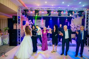 Wedding reception guests form a dance line under purple and blue lighting during celebration.