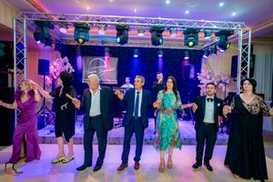 Wedding guests participate in a line dance under colorful stage lighting at reception venue.