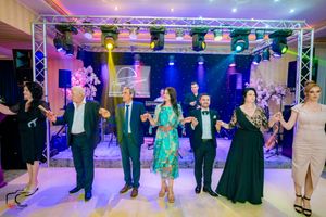 Party guests perform coordinated dance moves under dramatic purple and blue lighting.