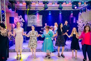 Wedding party members dance in formation during reception under colorful stage lighting.