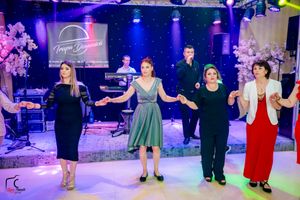 Performers in formal attire dancing in formation under theatrical lighting.
