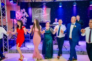 Dancers lined up in formal attire performing synchronized steps under dramatic blue stage lighting.