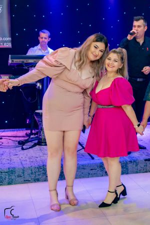 Two dancers in pink and beige outfits performing energetic dance moves on an illuminated floor.