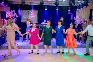 Festive dance performance with participants in bright dresses moving in formation under blue lights.