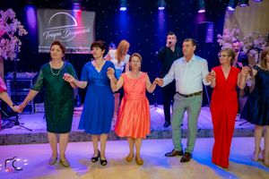Line dancers in colorful formal wear performing coordinated steps at an elegant venue.