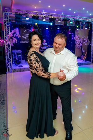 Couple dancing in formal attire under blue stage lighting at an event venue.