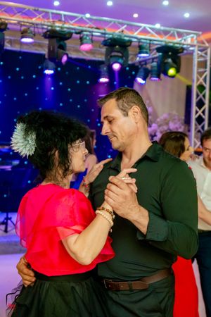 Dance partners in red and dark green outfits sharing an intimate moment on the dance floor.