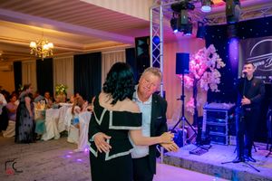 Couple dancing at elegant reception with purple lighting and white decor.