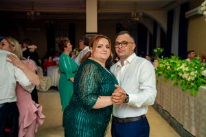 Dancing couple in emerald green dress and white shirt at formal celebration.