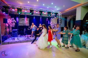 Wide shot of a dance floor with couples dancing under vibrant purple and blue lighting at an indoor venue.