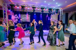 Panoramic shot of dancers performing in an indoor venue with dramatic purple and blue stage lighting.