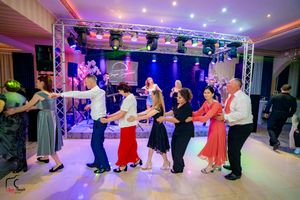 Dancers form a line while performing choreographed moves at an elegant ballroom event with colorful lighting.