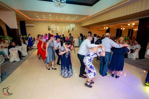 Panoramic view of a wedding reception with guests dancing under ornate chandeliers.