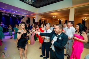Party guests dancing and celebrating in an elegant ballroom with purple mood lighting.