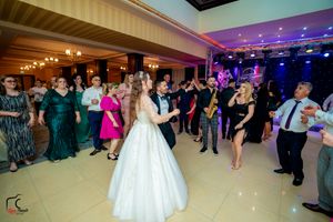 Panoramic view of a wedding celebration with guests dancing under purple and blue lighting in a grand ballroom.