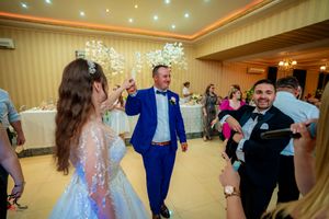 Wedding guests dancing and celebrating at an elegant reception with decorative lighting and striped wallpaper.