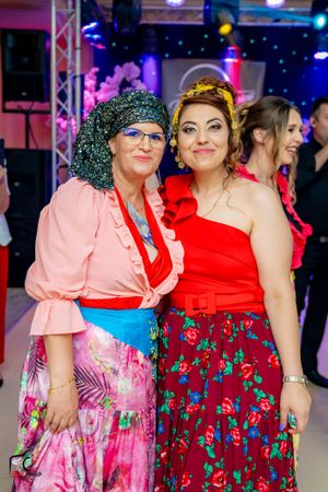 Group wearing bright floral dresses at an indoor celebration with stage lighting.