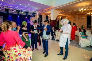 Wedding reception guests dancing and mingling in an elegant ballroom with purple mood lighting and chandeliers.