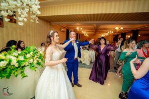 Wedding reception venue decorated with floral arrangements and chandeliers as guests dance.