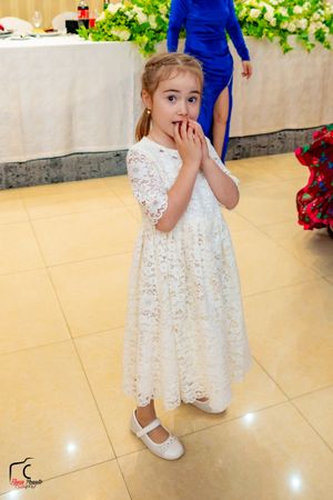 Young attendant in white lace dress walking across polished reception hall floor.