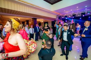 Panoramic view of a crowded dance floor with guests in formal wear under purple and blue lighting.