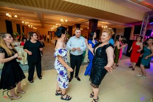 Large group dancing at a wedding reception in an elegant ballroom with chandeliers and stage lighting.
