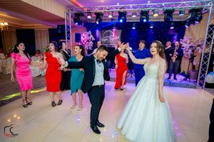 Elegant ballroom wedding reception with guests dancing under dramatic lighting and decorative truss setup.