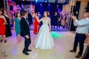 Wedding party and guests dancing in a beautifully lit ballroom with professional lighting effects.