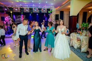 Wedding celebration with guests dancing in formal attire under purple stage lighting.