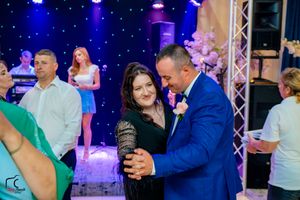 Multiple couples dancing at a formal event with colorful lighting and stage equipment visible.