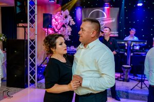 Couples dancing in formal attire at an event with dramatic lighting and stage equipment.