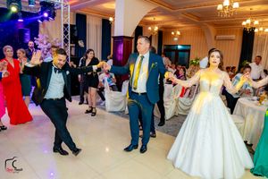 Wedding guests dance together in an elegantly lit ballroom with chandeliers and stage lighting.
