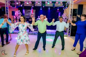 Group of wedding guests perform synchronized dance moves on illuminated dance floor.