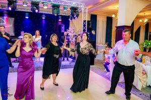 Wedding party members dance together during reception with purple and blue stage lighting.