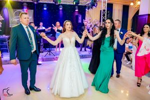 Celebratory dance line forms at a wedding reception with guests in formal attire under colorful lighting.