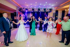Wedding reception guests dance together in a line formation under purple and blue lighting in an elegant ballroom.
