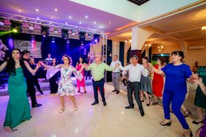 Large group of wedding guests participate in a synchronized dance line under vibrant purple lighting.