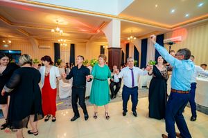 Wedding reception guests join hands in a festive dance line across the decorated ballroom floor.