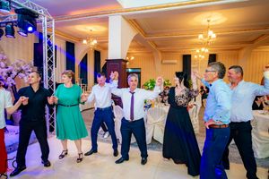 Wedding celebration features guests dancing in formation under dramatic purple and blue lighting.