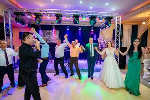 Wedding party and guests dance in formation under professional stage lighting in an elegant venue.