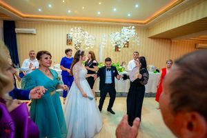 Wedding reception guests dancing and celebrating in an elegant ballroom with chandeliers and colorful lighting.