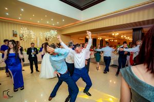 Wedding guests dancing energetically at a reception in an elegant ballroom with crystal chandeliers.