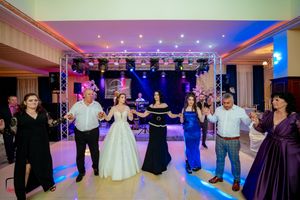 Wedding guests dance in a circle under colorful lighting and truss system at an elegant reception venue.