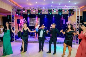 Formal party guests dance in a line under professional lighting at an indoor venue.